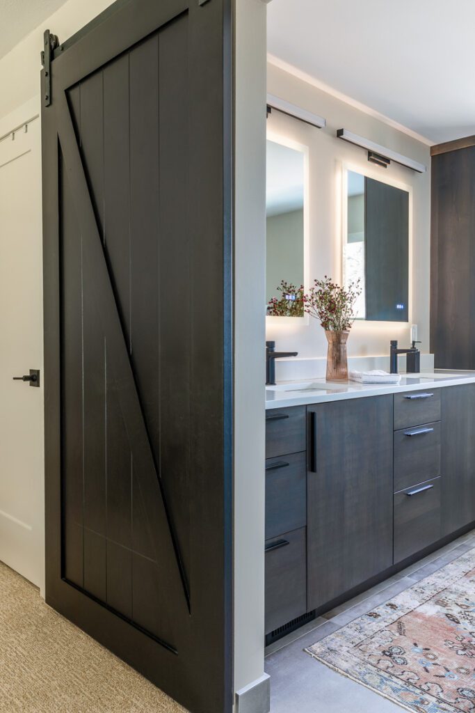 Custom bathroom cabinetry with clean lines, integrated storage, and a sliding barn door entry in classic contemporary primary bath design in Littleton main floor remodel by Denver Design Group