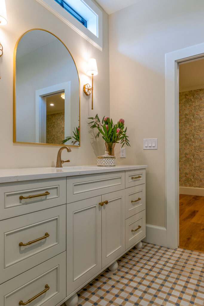 Child's bathroom with arched gold mirror, brass sconces, and gingham tile floor in Park Hill Denver remodel by Denver Design Group