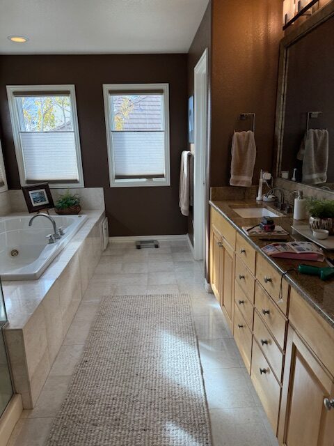 Builder-grade primary bathroom before remodel with dark brown walls and double vanity Littleton Colorado